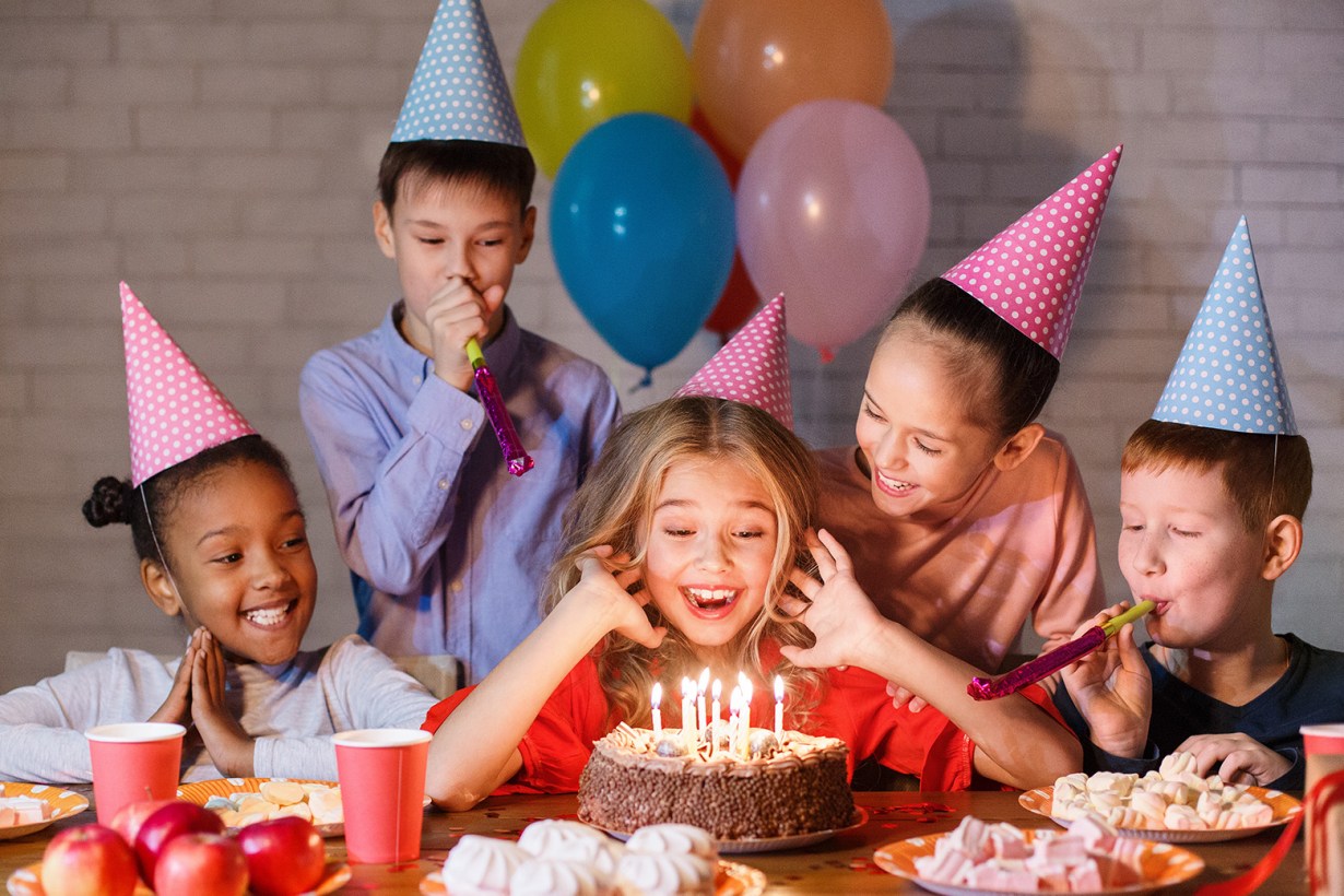 a young girl about to blow the birthday candles while surrounded by friends
